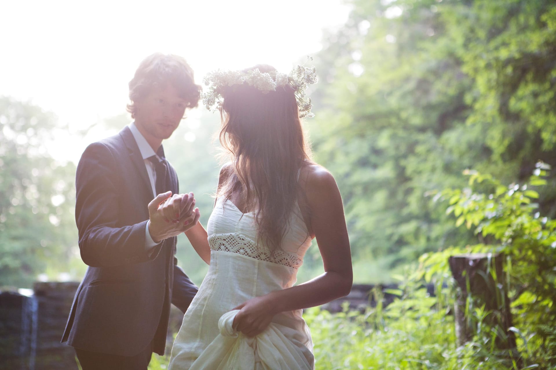 A groom leading his bride by the hand along a sunlit, tree-lined path
