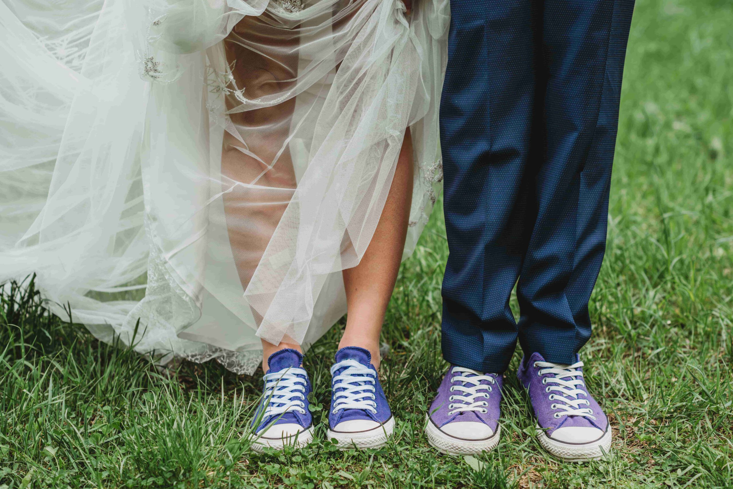 A couple in wedding attire wearing colourful trainers on grass